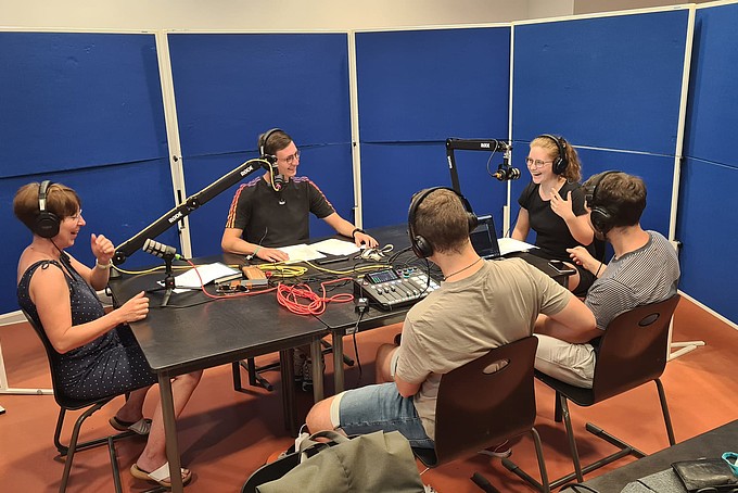 Beispielbild Podcastaufnahme: 5 Personen, 3 Sprecher mit Mikrofonen und 2 Menschen mit Aufnahmepult 